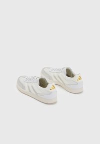 Baskets de sport blanches avec des accents gris, des panneaux texturés et un logo doré sur le talon. Dotées d'une semelle en caoutchouc et d'un système de laçage classique.