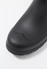 Botte en caoutchouc noire avec une finition lisse et mate ; bout arrondi ; semelle texturée pour une meilleure adhérence ; conçue pour une protection étanche.