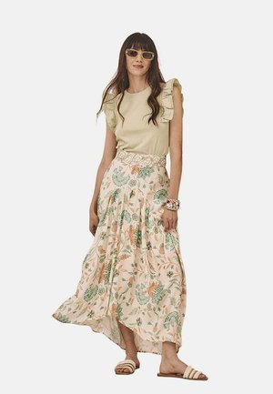 Top rizado de color verde claro combinado con una falda maxi floral en tonos pastel, acentuado por sandalias y accesorios beiges.