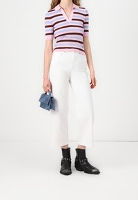 Pruhovaný pletený top v růžové, modré a hnědé barvě; bílé zkrácené džíny; texturované černé kotníkové boty se stříbrnými akcenty; drží modrou semišovou tašku.