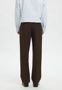 Rudos plačių kelnių kelnės su lygią tekstūrą, dėvimos su šviesiai mėlyna ir balta dryžuota palaidine. Kelnėse yra aukštas liemuo ir pritaikyta forma.