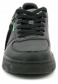 Zapatilla de cuero negra con punta redonda, suela plana negra, cordones negros y un acento verde. Presenta una cremallera en el lateral como detalle.