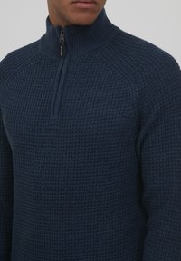 Jersey de lana azul marino con cuello alto con cremallera, superficie texturizada y mangas raglán, confeccionado con una tela suave y transpirable.