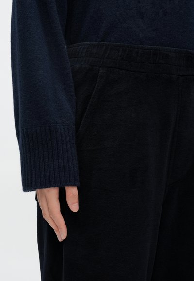 Πλεκτό πουλόβερ σε σκούρο μπλε με υφή, με ριμπ μανσέτες, συνδυασμένο με μαύρο παντελόνι από μαλακό ύφασμα, διαθέτοντας ελαστική μέση και πλαϊνές τσέπες.