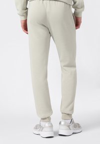 Pantalones de chándal gris claro, hechos de una tela suave, con una cintura elástica, piernas ajustadas y puños acanalados. Combinados con zapatos grises.