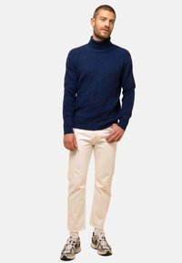 Suéter de cuello alto en color marino con un patrón hexagonal texturizado; combinado con pantalones blancos y zapatillas deportivas con un diseño en gris y negro.