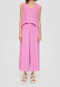 Růžový bezramínkový overal s volným střihem, který má nařasený pas a široké kalhoty. Nosit s chunky béžovými sandály.