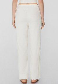 Pantaloni larghi bianchi con texture, orlo sfrangiato e vita elastica, mostrati da dietro. Indossati con sandali flat.