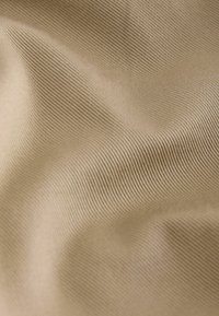 Tissu beige avec une texture fine côtelée verticale et de doux plis créant des ombres et des reflets subtils.