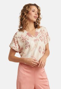 Lightweight, cream blouse with pink ikat pattern, V-neck, and rolled short sleeves. Paired with pink satin trousers.