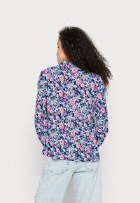 Casaco com padrão floral em fundo azul-marinho, apresentando flores rosas e turquesa, mangas longas e gola alta.