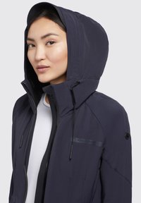 Giacca con cappuccio blu navy dal design elegante. Presenta coulisse regolabili, una chiusura con zip e un dettaglio logo sul petto.