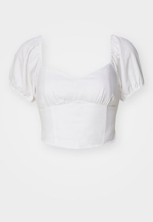 Fehér, puffos ujjú, rövidített felső, könnyű anyagból készült. Jellemzője a kerek dekoltázs és a redőzött részletek a mellen.