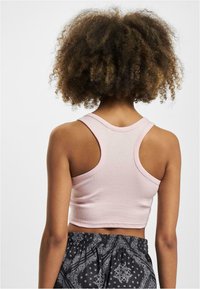 Rosa ribbet crop-top med racerback-design. Materialet er mykt og tettsittende, kombinert med svarte mønstrede shorts med elastisk midje.