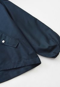 Marineblauwe jas met een slank ontwerp, gemaakt van zachte stof. Heeft een ronde mouw, een voorzak met drukknoopsluiting en een nette zoom.