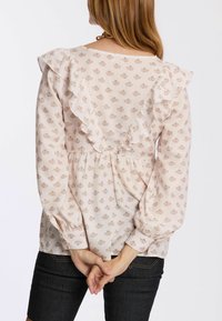 Helle rosa Bluse mit Rüschensaum auf der Rückseite, floralem Muster, langen Ärmeln und elastischen Bündchen. Der Stoff wirkt weich und leicht.