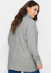 Maglione grigio a coste con colletto alto e maniche lunghe, caratterizzato da una vestibilità comoda e una texture morbida, indossato sopra un paio di jeans blu.