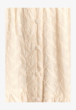 Embroidered cream blouse featuring a textured leaf pattern, five white buttons down the front, and a gathered hem.