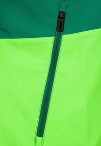 Jasně zelená bunda s tmavě zelenými detaily, obsahující kapsu na zip. Hladká textura s lehkou, prodyšnou konstrukcí látky.