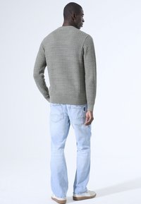 Texturiertes, hellgrünes Strickpullover mit Rundhalsausschnitt, kombiniert mit hellblauen, geraden Jeans und lässigen Schuhen, von hinten betrachtet.