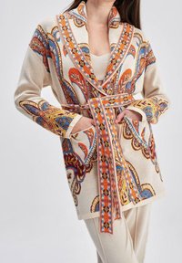 Cardigan à manches longues, à motifs crème avec des accents orange, bleu et doré. Doté d'un col châle, d'une ceinture et de poches avant.
