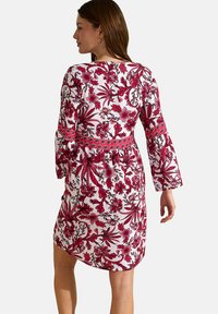 Robe à motifs floraux blancs, avec des motifs de feuillage rouges et roses, des manches longues, une taille cintrée et un col arrondi.