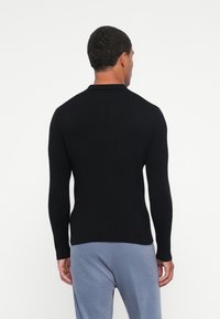 Schwarzer Langarm-Ripppullover mit Kragen und taillierter Passform. Trägt zu hellblauen Hosen, die die klaren Linien und Texturen betonen.