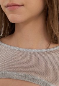 Primo piano della parte inferiore del viso di una donna, collo e spalla, che indossa un top in rete metallica argento con capelli castani visibili di lato.