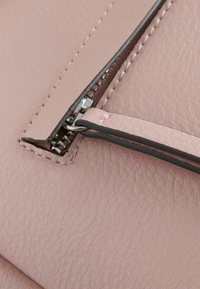 Gros plan d'une fermeture éclair métallique partiellement ouverte sur un cuir rose texturé avec des coutures visibles et une languette en cuir assortie.