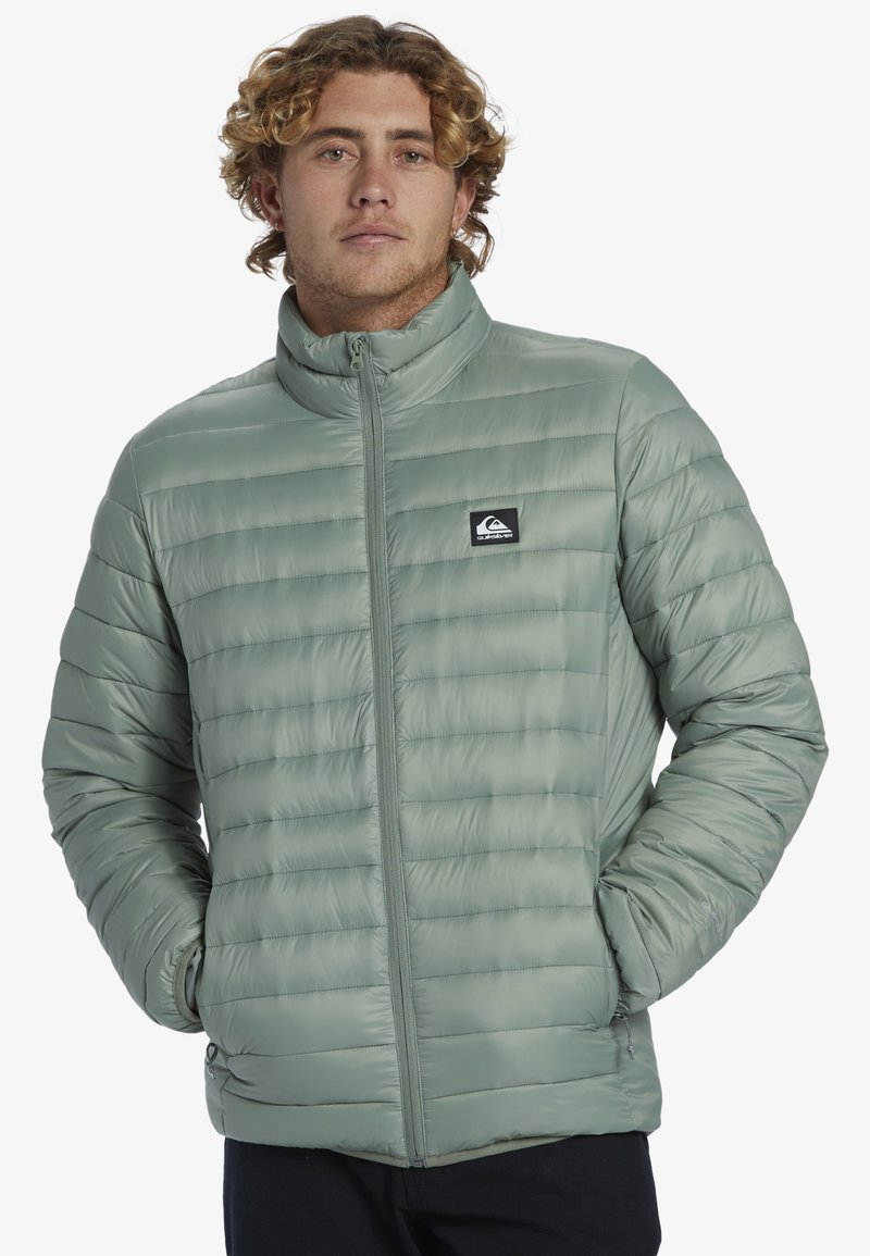 Hellgrüne Pufferjacke mit hohem Kragen, horizontal gestepptem Design, Frontreißverschluss und Logopatch auf der linken Brust. Weiche, glatte Textur.