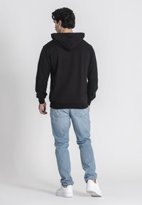 Sudadera negra con capucha ajustable, combinada con unos jeans de mezclilla azul claros. Presenta puños y dobladillo acanalados, y se lleva con zapatillas blancas.