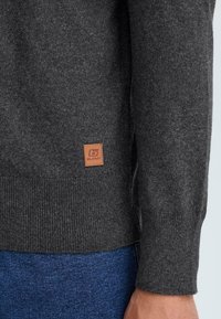 Dunkelgrauer Pullover aus Strickstoff, mit gerippten Bündchen und strukturiertem Finish. Beinhaltet ein kleines braunes Lederetikett am Saum.