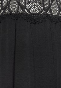 Melna kleita ar teksturētu mežģīņu pārklājumu augšējā daļā. Audums ir gluds ar plūstošu apakšējo daļu un sarežģītu mežģīņu izšuvumu.