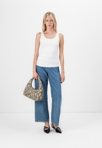 Witte tanktop, blauwe wijde jeans en zwarte hakken. Een beige handtas met een patroon en een gebogen vorm maakt de look compleet.