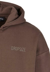 Hnedá mikina s kapucňou vyrobená z jemného materiálu. Obsahuje tónový logo "DROPSIZE" na prednej strane a klasický dizajn kapucne.