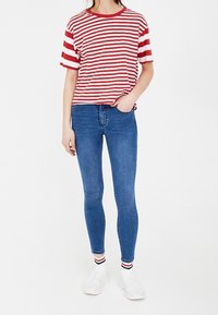 Camiseta de manga corta a rayas rojas y blancas combinada con jeans ajustados azules. Zapatillas blancas y calcetines con rayas rojas y azules visibles.