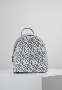 Grå och vit tygryggsäck med en böjd form, med ett geometriskt mönster, handtag på toppen och en dragkedjestängning på sidan.