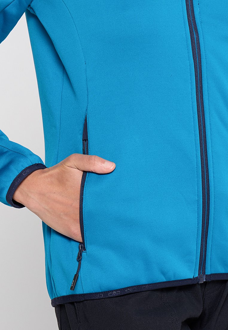 Blaue Softshell-Jacke mit einem Reißverschluss auf der Vorderseite, marineblauen Akzenten, einer Seitentasche und elastischen Bündchen für einen sicheren Sitz. Glatte, leichte Textur.
