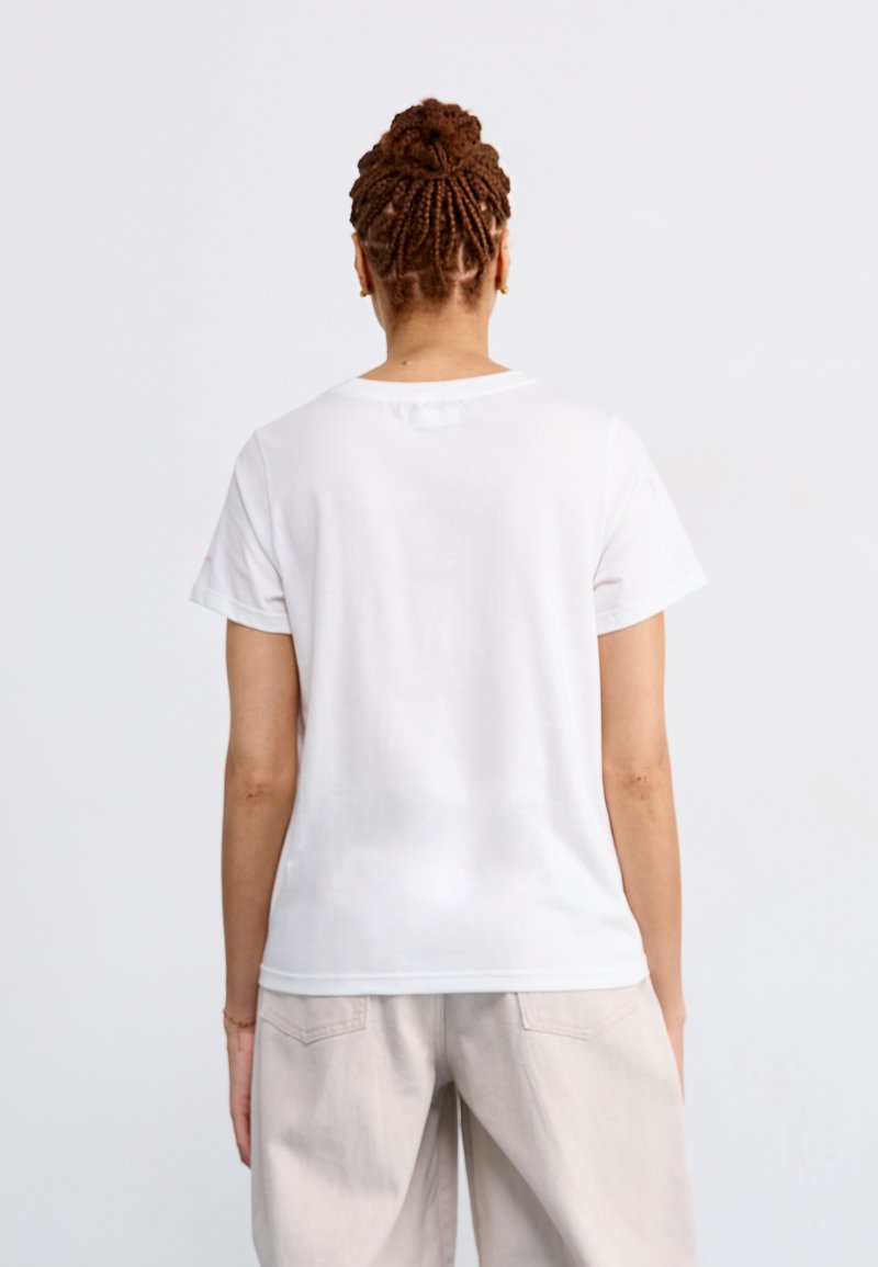 Weißes Baumwoll-T-Shirt mit kurzen Ärmeln, rundem Halsausschnitt und glatter Textur. Keine sichtbaren Muster oder Grafiken, getragen mit hellen Hosen.