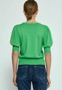 Leuchtend grüner Pullover mit puffierten kurzärmeligen und einem gerippten Saum, kombiniert mit dunkelblauen Jeans. Glatte Textur, einfaches Design.