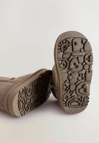 Bruna mockaskinnankelhöga stövlar med texturerade gummisulor som har lekfulla mönster, inklusive hjärtan och leende ansikten.