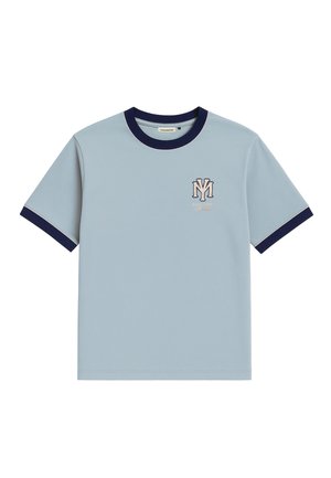 Uomo che indossa una maglietta azzurro chiaro con bordo scuro, bandana blu scuro intorno al collo, pantaloni grigi a righe sottili e cappellino blu scuro con scritta bianca.