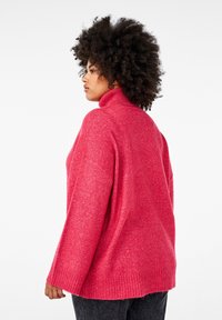 Rosa ullpolotröja med lös passform, texturerad yta och ribbade mudd- och nederkanter. Buren över mörka jeans, visande bakifrån.