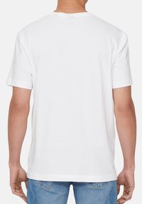 Weißes Baumwoll-T-Shirt mit kurzen Ärmeln, lockerer Passform, runder Ausschnitt und glatter Textur, von hinten betrachtet, kombiniert mit blauen Jeans.