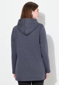 Šedá mikina s kapucí, měkký materiál, volný střih a dlouhé rukávy. Zadní část má kapuci a zaoblený spodní lem.