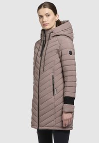 Polstret lang jakke i afdæmpet mauve med chevron-stikninger, hætte, høj krave, lynlåslommer og sorte strikkede manchetter.
