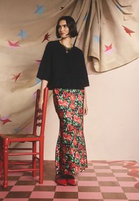 Pulover negru, pufos, cu mâneci scurte, asortat cu o fustă lungă, florală, decorată cu trandafiri roșii pe un fundal verde. Pantofii roșii completează ținuta.