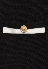Tissu tricoté noir avec un petit détail de poche à rayure blanche horizontale, fixé par un bouton décoratif rond doré.