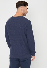 Granatowy sweter z dzianiny z teksturowanym wzorem w romby, z prążkowanymi mankietami i dołem. Posiada okrągły dekolt i luźny krój.