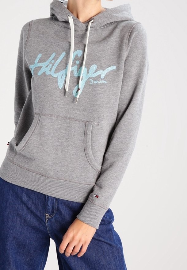 Sweat à capuche en coton gris avec un logo bleu "Hilfiger Denim", capuche à cordon, poche kangourou et poignets côtelés. Porté avec un jean bleu.